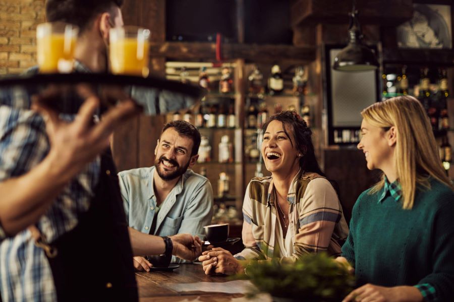 Vrienden zitten in de horeca op een pvc-vloer en krijgen een drankje.
